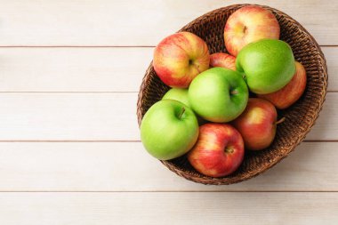 Fresh ripe red and green apples in wicker bowl on light wooden table, top view. Space for text