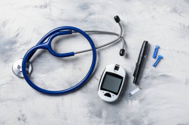 Diabetes. Digital glucometer, pen, test strip, lancets and stethoscope on gray textured table, flat lay