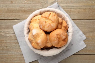 Delicious freshly baked buns in bowl on wooden table, top view