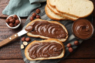 Çikolata ezmeli tostlar, fındıklı fındıklar ve tahta masa üzerinde bıçak, düz uzanma