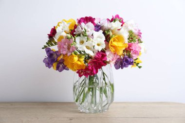 Güzel frezya çiçekleri cam vazoda, ahşap masada, beyaz duvarın yanında.