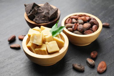 Organik kakao yağı, fasulye, çikolata parçaları ve yeşil yapraklar siyah masada, yakın plan.