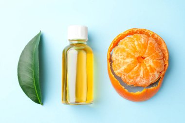 Bir şişe mandalina esaslı yağ, açık mavi arka planda yaprak ve meyve, düz uzanmış.