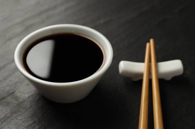 Soya sosu kasede ve çubuklar siyah masada, yakın plan.