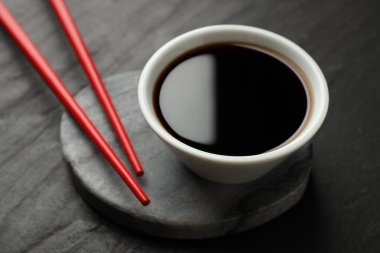 Soya sosu kasede ve çubuklar siyah masada, yakın plan.
