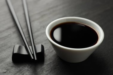 Soya sosu kasede ve çubuklar siyah masada, yakın plan.