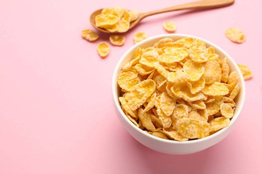 Lezzetli mısır gevrekleri kasede ve kaşık pembe arka planda, yakın plan. Metin için boşluk