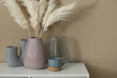 Güzel vazolar çiçek dekoru ve mum tutacağı bej duvarın yanındaki beyaz dolapta, yakın plan. Metin için boşluk