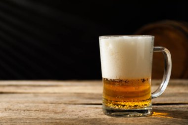 Ahşap masada taze bira ve koyu arka planda fıçı, yakın plan. Metin için boşluk