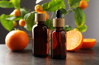 Mandalina yağı şişeleri ve gri masada taze meyveler, yakın plan.