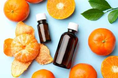 Bir şişe mandalina yağı ve açık mavi arka planda meyveler.