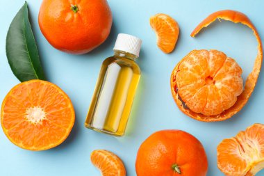 Bir şişe mandalina esaslı yağ ve açık mavi arka planda meyveler.