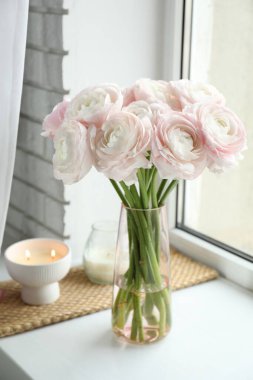 Güzel ranunculus çiçekleri cam vazoda ve beyaz pencere pervazında yanan mumlar.