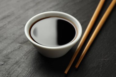 Soya sosu kasede ve çubuklar siyah masada, yakın plan.
