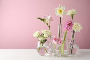 Beyaz masadaki vazolarda pembe arka planda farklı güzel çiçekler. Metin için boşluk