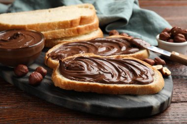 Çikolata ezmeli tostlar, fındıklı fındıklar ve tahta masada bıçak, yakın plan.