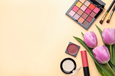 Farklı makyaj ürünleri ve bej arka planda güzel çiçekler. Metin için boşluk
