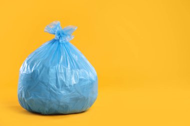 Açık mavi çantadaki çöpler sarı arka planda, yakın plan. Metin için boşluk