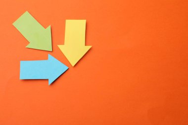 Turuncu arka planda renkli kağıt oklar, düz yatış. Metin için boşluk