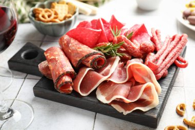 Şarküteri tahtası, farklı pişirilmiş et, sosis ve şarap beyaz fayanslı masada, yakın plan.