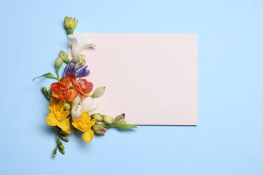 Different colorful flowers and blank paper on light blue background, flat lay. Space for text