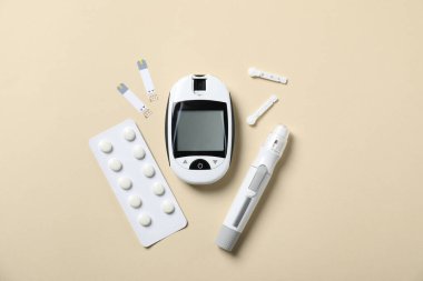 Diyabet. Dijital glukometre, kalem, mızraklar, test şeritleri ve bej arka plandaki haplar, düz konum