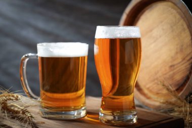 Taze biralı bardaklar, masaya çiviler ve fıçı, koyu arka plan, yakın plan.