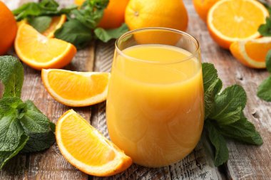 Citrus suyu bardakta, taze portakal ve nane yaprakları ahşap masada, yakın plan.