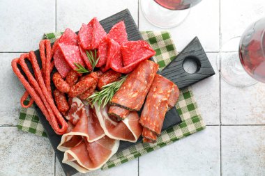 Şarküteri tahtası, farklı pişirilmiş et, sosis ve beyaz fayanslı masa üzerinde şarap.