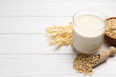 Bardakta yulaf sütü, beyaz ahşap masada tanecikler ve çiviler, yakın plan. Metin için boşluk