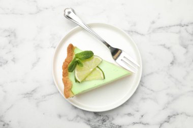 Beyaz mermer masa üzerinde çatal ve nane ile nefis bir dilim limonlu turta.