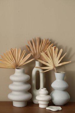 İçerideki bej duvarın yanındaki ahşap masada kurutulmuş palmiye yaprakları olan güzel vazolar.