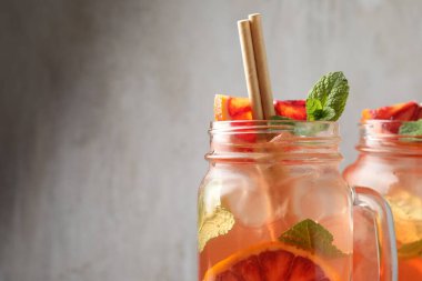 Sicilya portakallı lezzetli bir içecek, buz küpleri ve bulanık gri arka planda naneli kavanozlar, yakın plan. Metin için boşluk