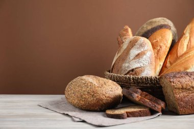 Hasır sepetteki farklı ekmek somunları kahverengi arka plana karşı ahşap masada, yakın plan. Metin için boşluk