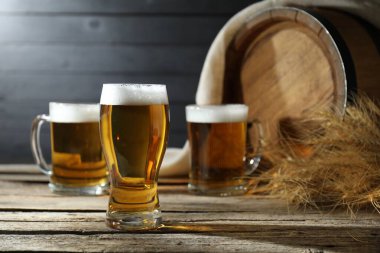 Taze biralı bardaklar, çiviler ve tahta masanın üzerinde koyu arka planda duran fıçılar.