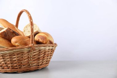 Açık gri masada hasır sepetteki farklı ekmek türleri, yakın plan. Metin için boşluk