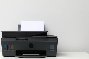 Açık gri duvarın yanında üzerinde beyaz ahşap masa olan siyah bir yazıcı, yakın plan. Metin için boşluk