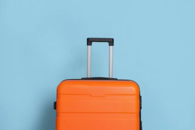 Açık mavi arkaplanda turuncu bir bavul, yakın plan.