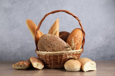 Farklı türde ekmek somunları ve hasır sepetteki buğday çivileri ahşap masada, yakın plan.
