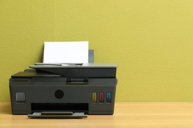 Kapalı alandaki yeşil duvarın yanındaki ahşap masanın üzerinde kağıt olan siyah bir yazıcı. Metin için boşluk