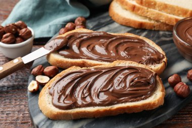 Çikolata ezmeli tostlar, fındıklı fındıklar ve tahta masada bıçak, yakın plan.