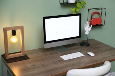 Stylish workplace with modern computer, lamp, houseplant and stationery on wooden table indoors
