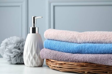 Stack of colorful terry towels, sponge and cosmetic product on table near light wall