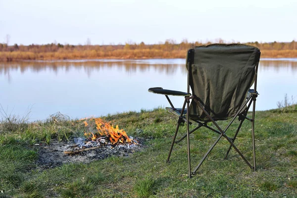 Tourist chair, folding chair, bonfire on the river bank in autumn at sunset, relaxation and rest, early autumn, close-up, copy space