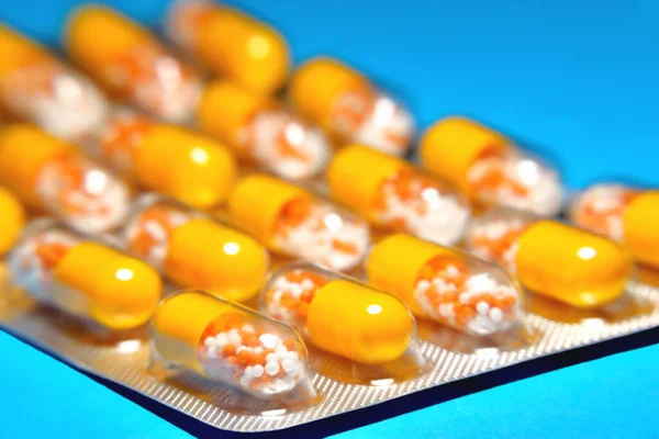 capsules in a blister, a medicine, tablets, vitamins in the form of granules in a yellow capsule, blur as a creative technique of the author, close-up and copy-space