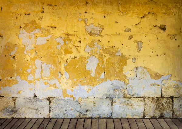 Rough wall with peeling yellow paint and wooden floor — Stock Photo, Image