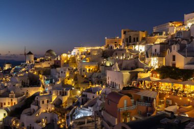 Yunanistan 'ın Santorini kentindeki Oia Köyü' nün Atmosferik Gece Manzarası, Geleneksel Evleri Sıcak Işıklar Aydınlatıyor