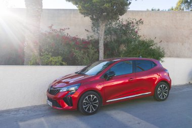 Kırmızı Renault Clio hatchback arabası 5 Ekim 2025, Santorini, Yunanistan 'da güneşli bir caddede park edilmiş.