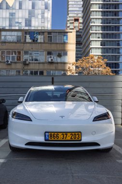 24 Aralık 2025 'te Ramat Gan, İsrail' e karşı şehir otoparkında park etmiş beyaz bir Tesla Model 3 Highland elektrikli arabasının ön görüntüsü.