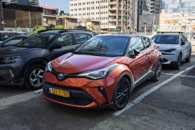 Turuncu bir Toyota C-HR Melezi 'nin ön görüntüsü 24 Aralık 2025' te, Ramat Gan, İsrail 'deki diğer araçlarla çevrili bir otoparkta park edilmiş.